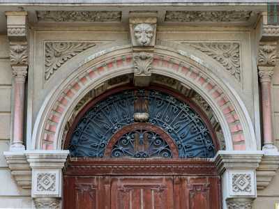Ci avviciniamo al grande portone in legno, con lunettone ornato in ferro battuto, delimitato da due esili colonne corinzie con dadi brunelleschiani sui capitelli. Queste reggono un ampio archivolto dentellato, decorato con motivi vegetali nell�interno e con una testa felina in chiave